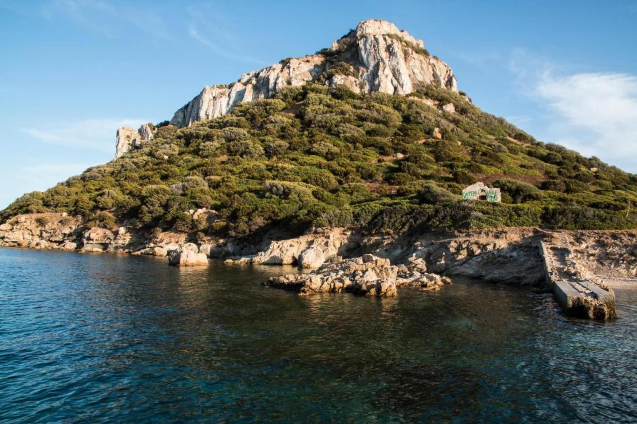 Paesaggio costiero con una collina rocciosa e un piccolo edificio sulla cima.