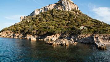 Paesaggio costiero con una collina rocciosa e un piccolo edificio sulla cima.