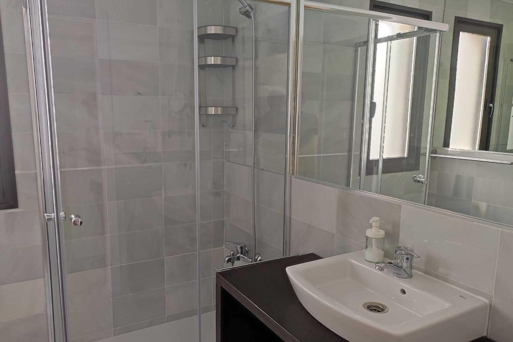 Ein modernes Badezimmer mit einer gläsernen Dusche, einem weißen Waschbecken und einem großen Spiegel.
