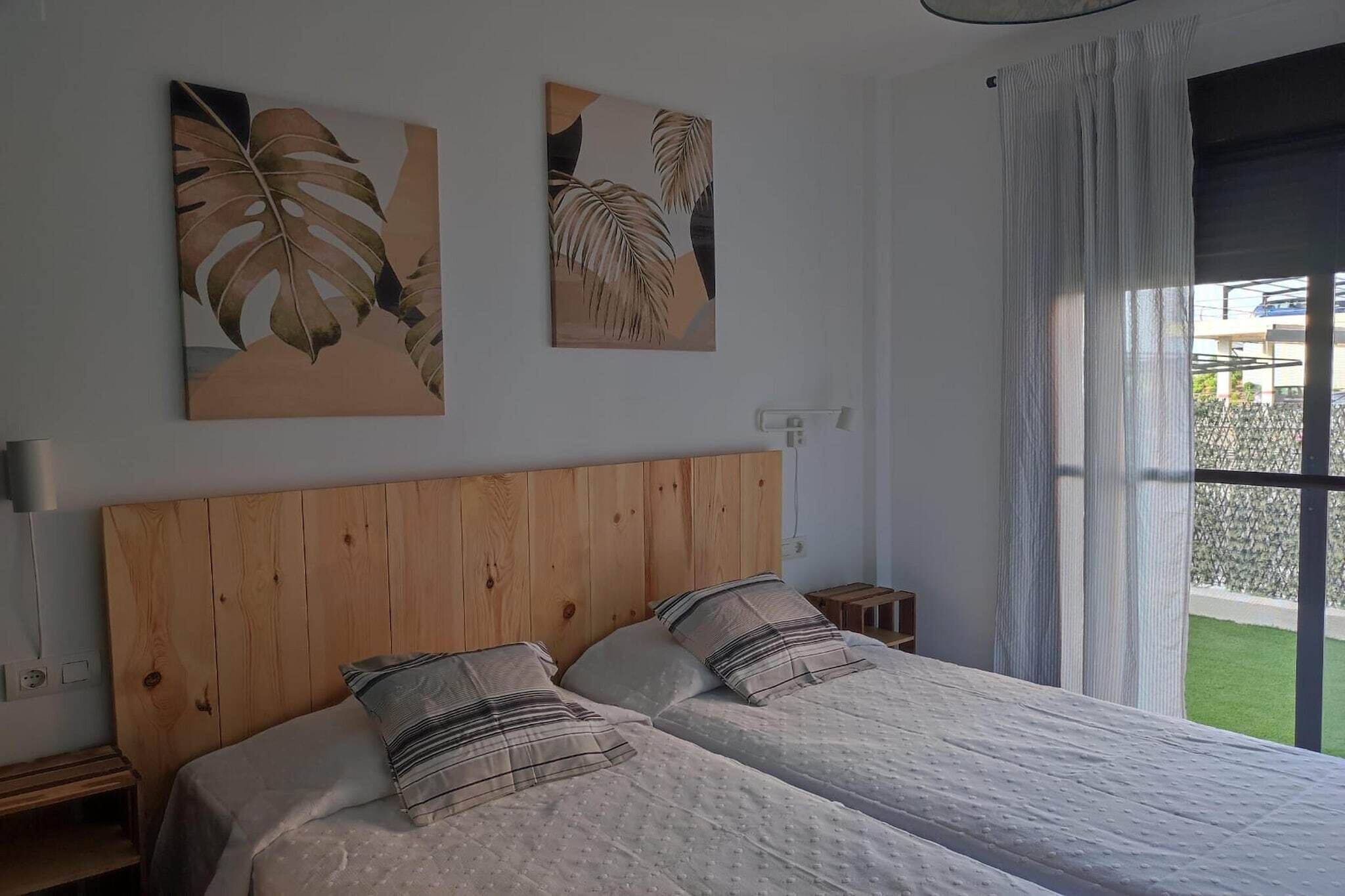 A bedroom with a wooden headboard, two beds with striped bedding, and two wall-mounted paintings of leaves.