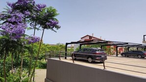 Ein Parkplatz mit zwei Autos, einer Überdachung und einem Baum mit violetten Blüten.