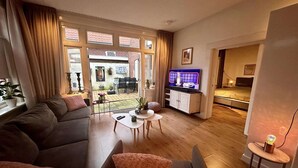 Ein modernes Wohnzimmer mit einer Couch, einem Couchtisch und einem Fernseher. Durch die Glastüren ist ein Essbereich zu sehen.