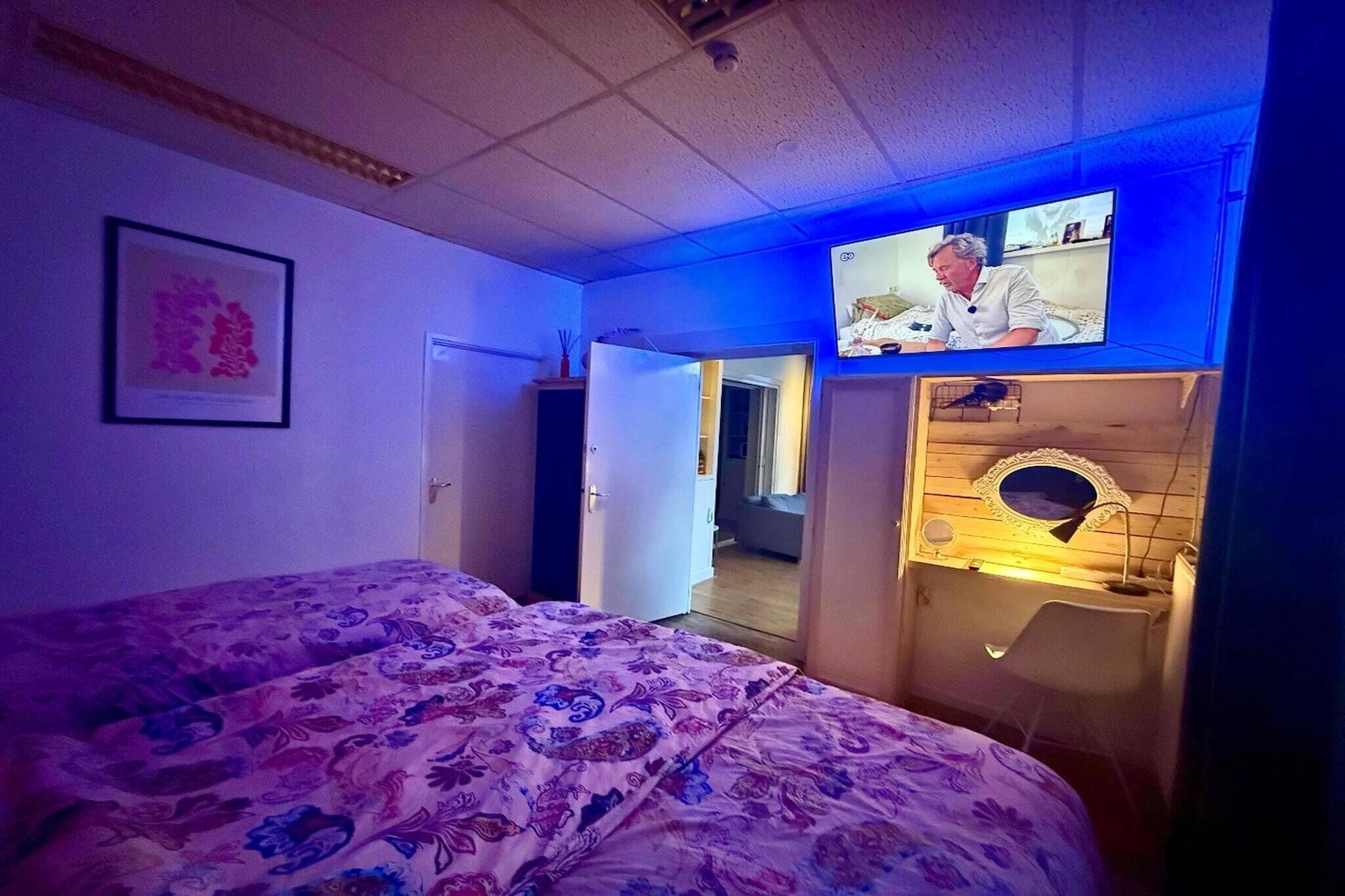 Een slaapkamer met een bed, een aan de muur bevestigde televisie en een deur naar een andere kamer.