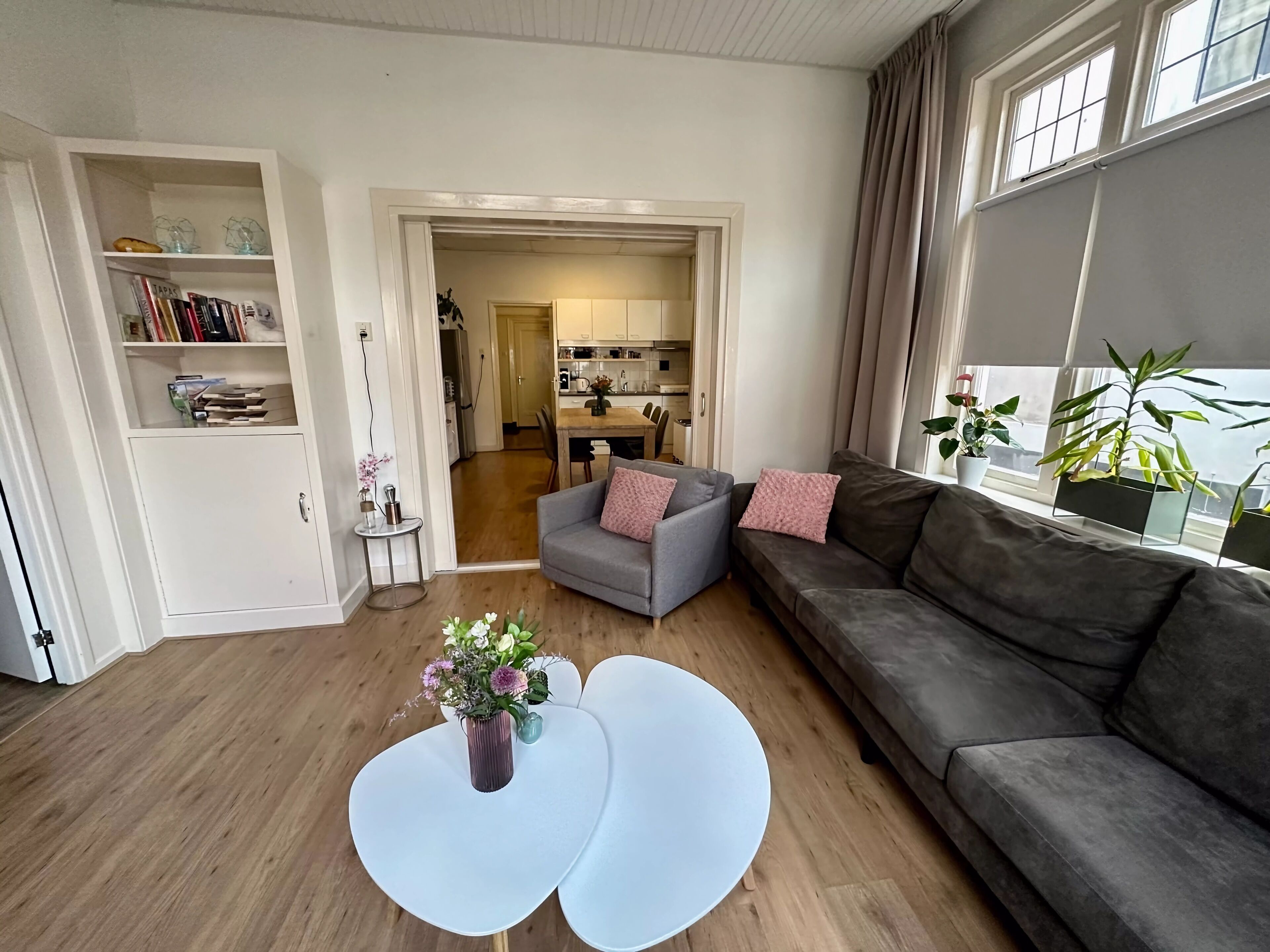 Een moderne woonkamer met een grijze bank, een witte salontafel en een boekenkast.