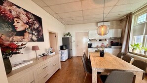 Eine moderne Küche mit weißen Schränken, einem Holzes Esstisch und einem großen floralen Gemälde an der Wand.