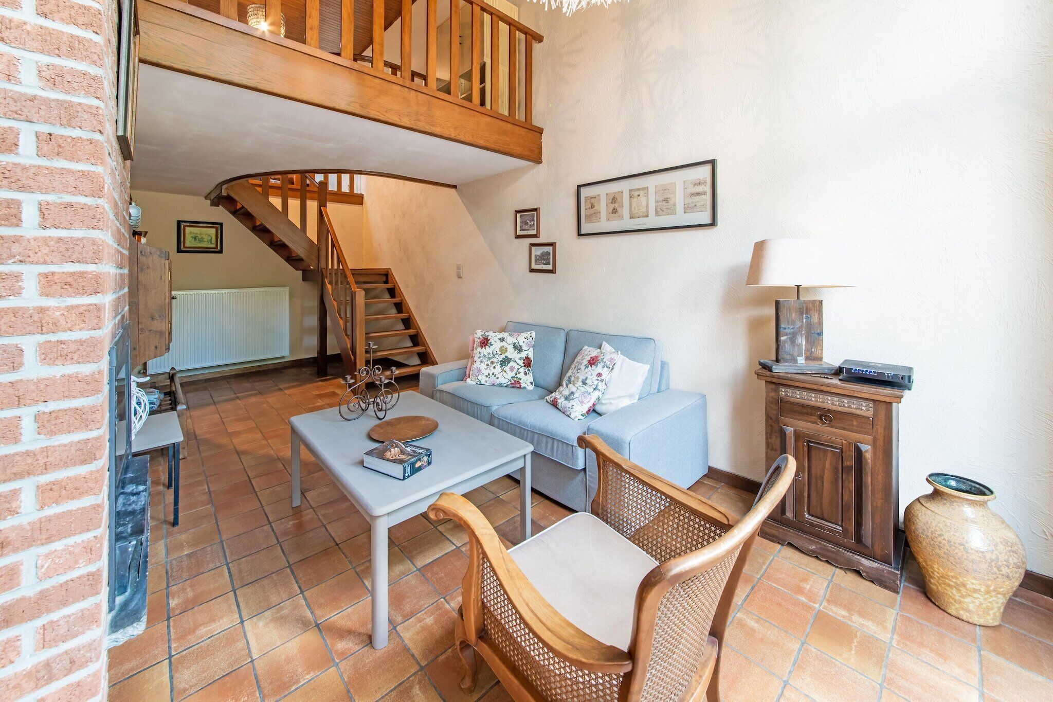 Un salon chaleureux avec un escalier en bois, un canapé bleu, une table basse, des fauteuils en osier et un meuble en bois.