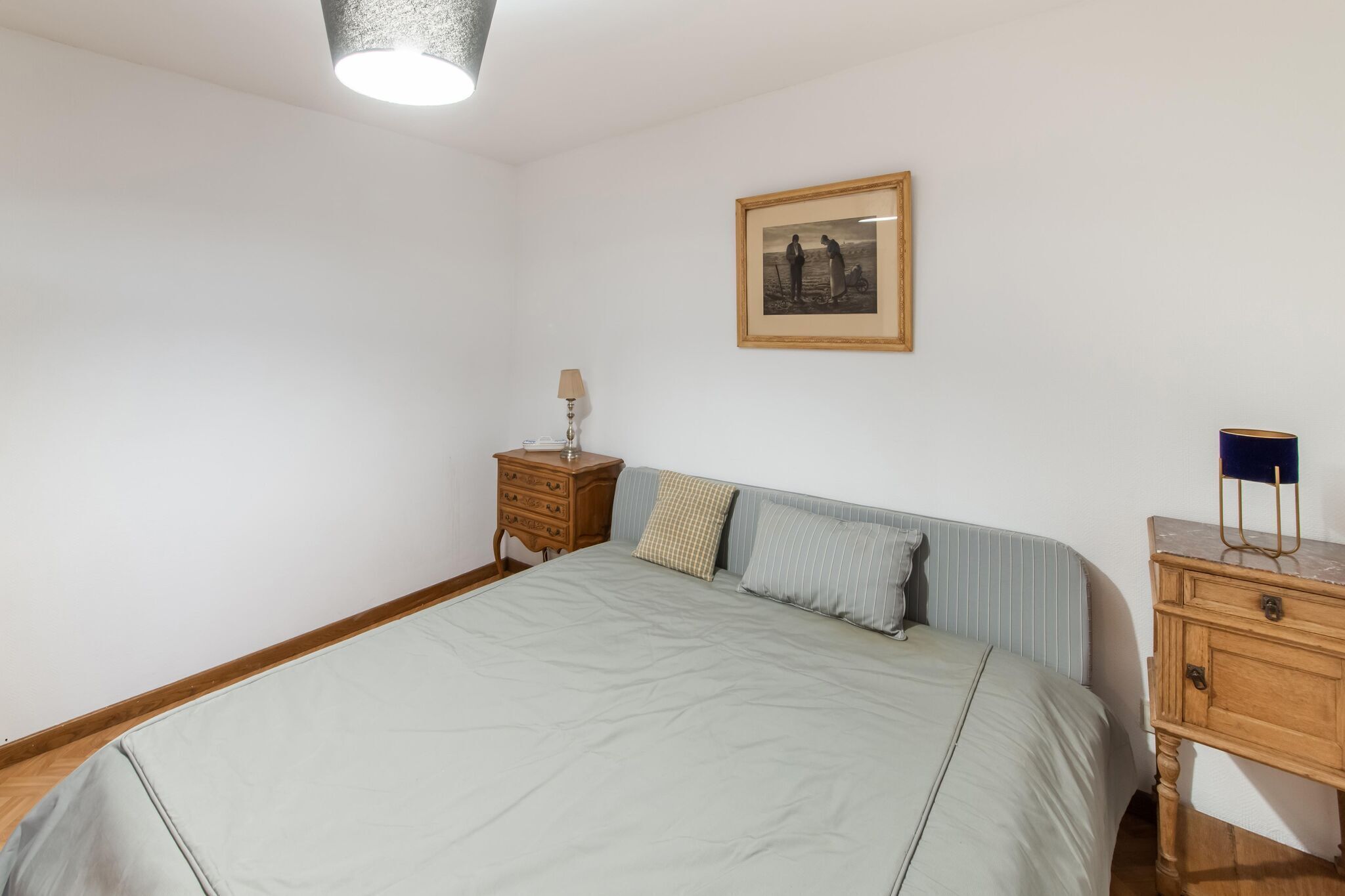 A bedroom with a bed, a nightstand, a dresser, a lamp, and a framed picture on the wall.