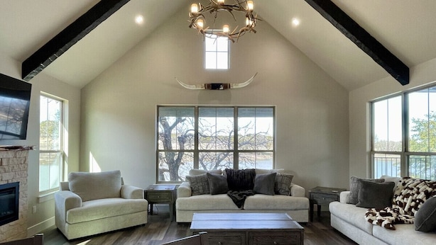 A spacious living room with a high ceiling, large windows, and a fireplace.
