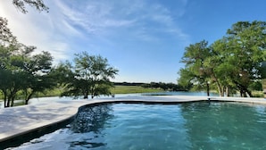 A swimming pool with a curved edge, surrounded by trees and a clear sky.