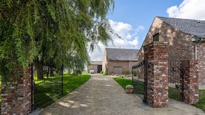 A paved pathway leading to a brick building with a metal gate, surrounded by greenery and a clear sky.