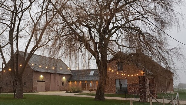 A rustic barn with string lights, a picnic table, and a fenced area.