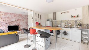 A modern kitchen with a central island, bar stools, a washing machine, and a microwave. - Sunlit Garden Escape Normandy (Isigny sur Mer)