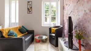 A modern living room with a sofa, armchair, and coffee table, a flat-screen TV, and a window with a view of greenery. - Sunlit Garden Escape Normandy (Isigny sur Mer)
