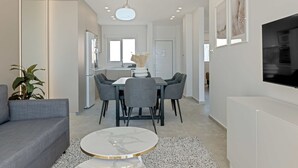 A modern living room with a grey sofa, a round coffee table, and a dining area with a white table and grey chairs. - Phaedrus Living: Seaview Luxury Flat Limnaria 150 (Paphos)