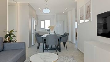 Una sala de estar moderna con un sofá gris, una mesa de centro redonda y un comedor con mesa blanca y sillas grises.