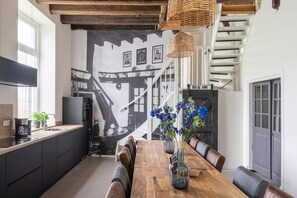 Enjoy meals at the dining table with cushioned benches, surrounded by a black and white mural and a staircase.