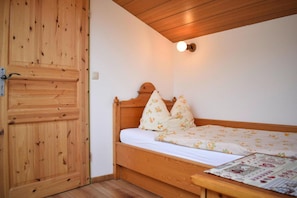 A wooden bed with floral bedding, a wooden door, and a wall-mounted light fixture.