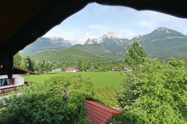 A mountain view from a covered outdoor area with a red-roofed building in the foreground.