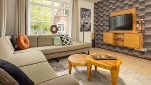 A modern living room with a sofa, a wooden coffee table, and a TV mounted on a geometric-patterned wall. - Holiday Villa with Garden (Bad Bentheim)