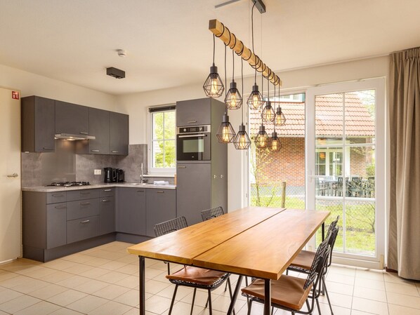 A modern kitchen with grey cabinets, a wooden dining table, and a large window with a view of a brick house.