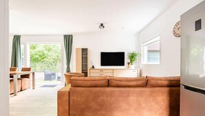 A modern living room with a brown sofa, a flat-screen TV, and a dining area with a table and chairs. - Charming holiday home in Poortugaal with garden (Poortugaal)