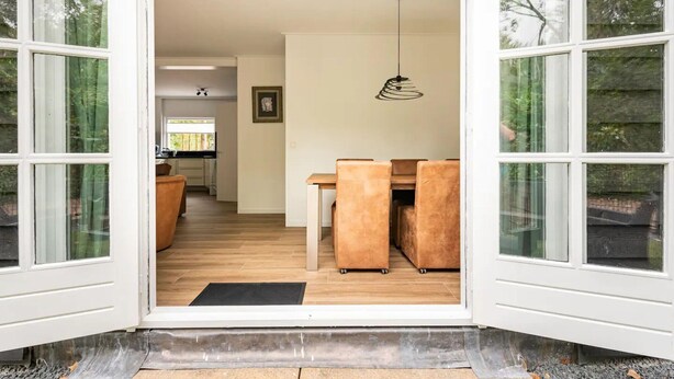An open doorway leading to a dining area with a wooden table and chairs, a hanging light fixture, and a view of a kitchen in the background. - Charming holiday home in Poortugaal with garden (Poortugaal)
