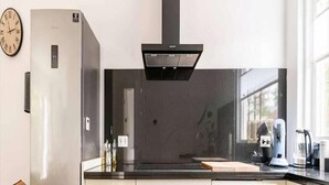 A modern kitchen with a stainless steel refrigerator, a built-in oven, a black range hood, and a window providing natural light. - Charming holiday home in Poortugaal with garden (Poortugaal)