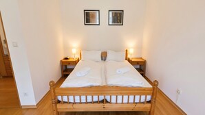 Cama doble con cabecera y piecera de madera, dos mesitas de noche con lámparas y dos cuadros enmarcados en la pared.