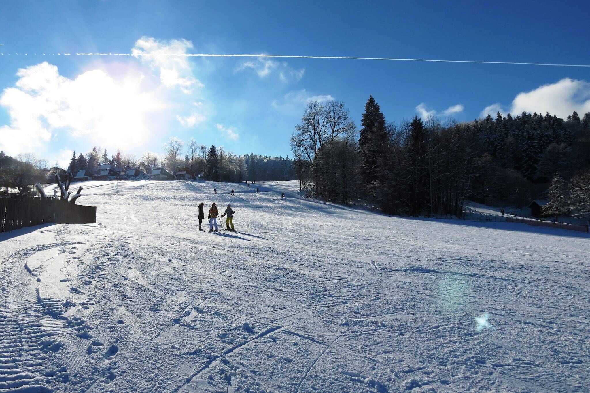 Ein verschneiter Skipisten mit blauem Himmel und Bäumen im Hintergrund.