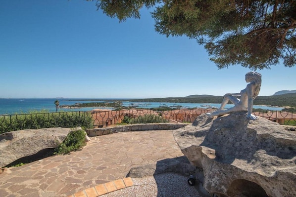 Un patio de piedra con una estatua que domina un paisaje costero.