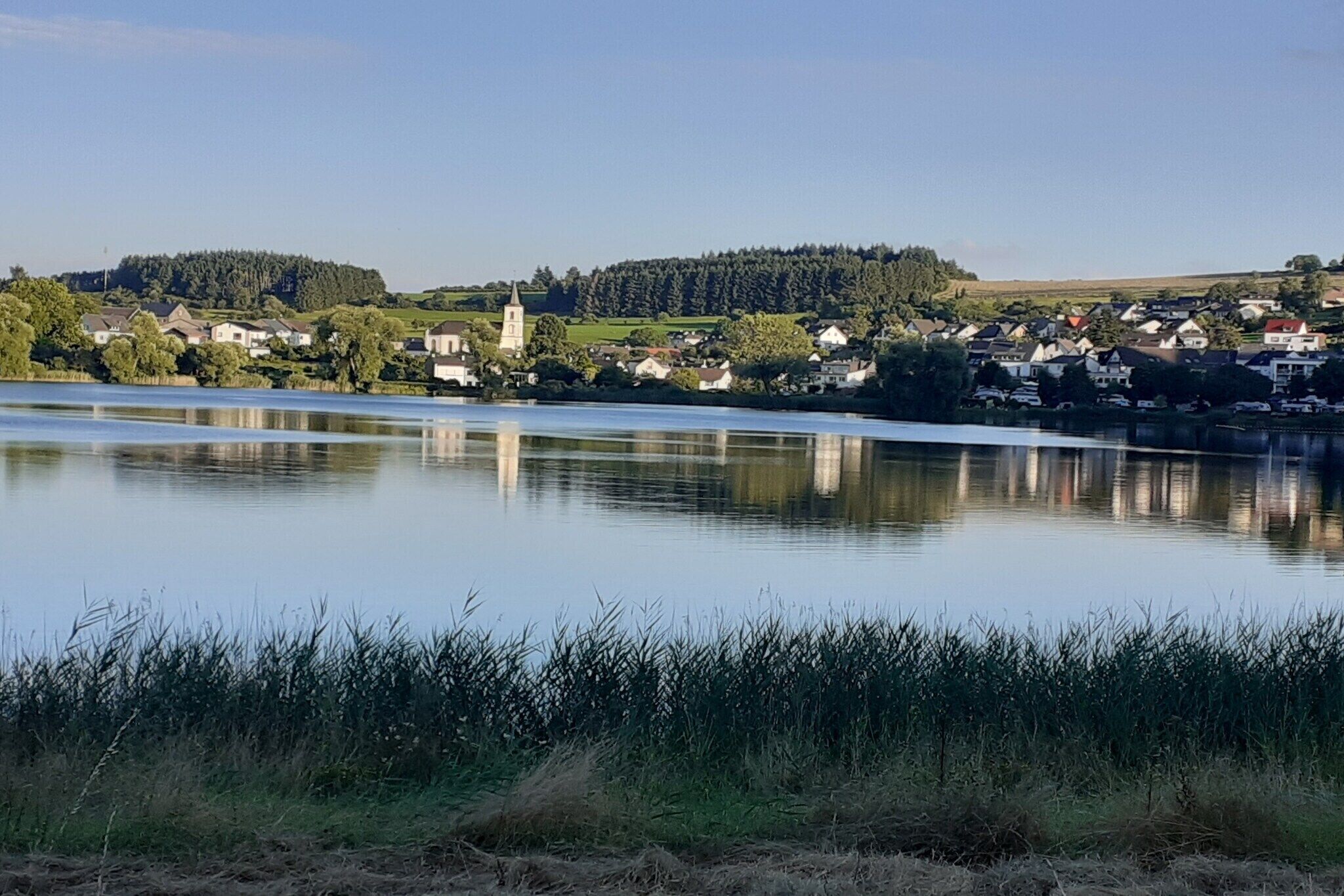 A calm lake with a church and residential buildings in the background.
