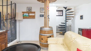 Un salon moderne avec une fresque représentant un paysage urbain, une colonne en forme de tonneau en bois, un escalier en colimaçon et un canapé beige.