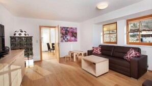 A modern living room with a brown sofa, a wooden coffee table, and a dining area with a small table and chairs. There is a kitchen area with cabinets and a refrigerator. - Apartment Wald im Pinzgau near Ski Lift (Wald im Pinzgau)