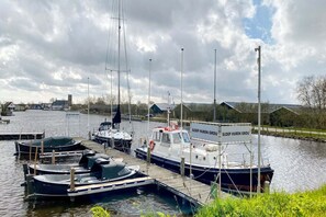 Een jachthaven met diverse boten afgemeerd bij houten steigers, een bord met de tekst 'SLOEP HUREN GROU' en een bewolkte lucht op de achtergrond.