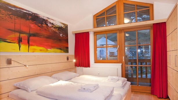 Habitació amb dos llits, un quadre a la paret, una finestra amb cortines vermelles i vista a l'exterior.