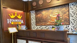 A reception area with a wooden reception desk, a crown logo, and a wall with clocks and city names. - Hoang Gia Hotel Dong Tru -by Bay Luxury (Hanoi)
