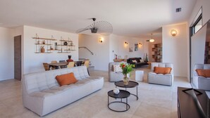 A modern living room with a sofa, coffee table, and a dining area with chairs and a table. - Superb villa with pool and sea view (Monticello)