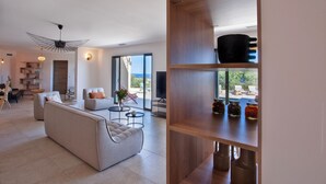 A modern living room with a sofa, coffee table, and a wooden shelf with jars. - Superb villa with pool and sea view (Monticello)