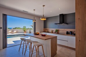 Une cuisine moderne dotée d’un grand îlot central, de tabourets de bar et offrant une vue sur une piscine et un espace de détente extérieur.