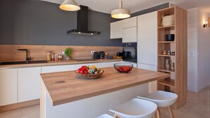A modern kitchen with a wooden countertop, white cabinets, and a built-in oven. There are two pendant lights, a black range hood, and a wooden shelf with jars. - Superb villa with pool and sea view (Monticello)