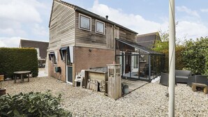 A modern house with a patio area, a covered outdoor seating area, and a glass-enclosed room.