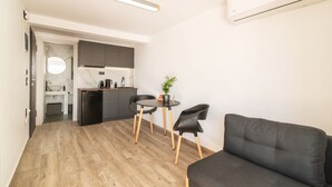 Un espace de vie compact comprenant un coin cuisine, un coin repas avec deux chaises, un canapé et une plante en pot.