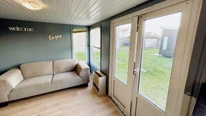 A modern living room with a beige sofa, a 'welcome' sign, and a 'Enjoy' sign on the wall. - Lovely holiday home in Vlaanderen with garden (Vlaanderen)