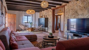 Ein modernes Wohnzimmer mit einer Steinwand, Holzbalken, einem großen Flachbildfernseher und einer gemütlichen Sitzecke mit Sofa und Sesseln.