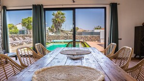 Ein Holztisch mit gewebten Platzsets, umgeben von Korbstühlen, mit Blick auf einen Pool und einen Außenbereich.