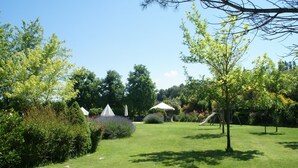 A well-maintained garden with a grassy lawn, several trees, and a white gazebo.