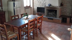 A dining area with a wooden table and chairs, a stone wall, a fireplace, and a television.