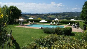 A pool area with lounge chairs and umbrellas, surrounded by well-maintained lawns and hedges, with a scenic mountain view in the background.