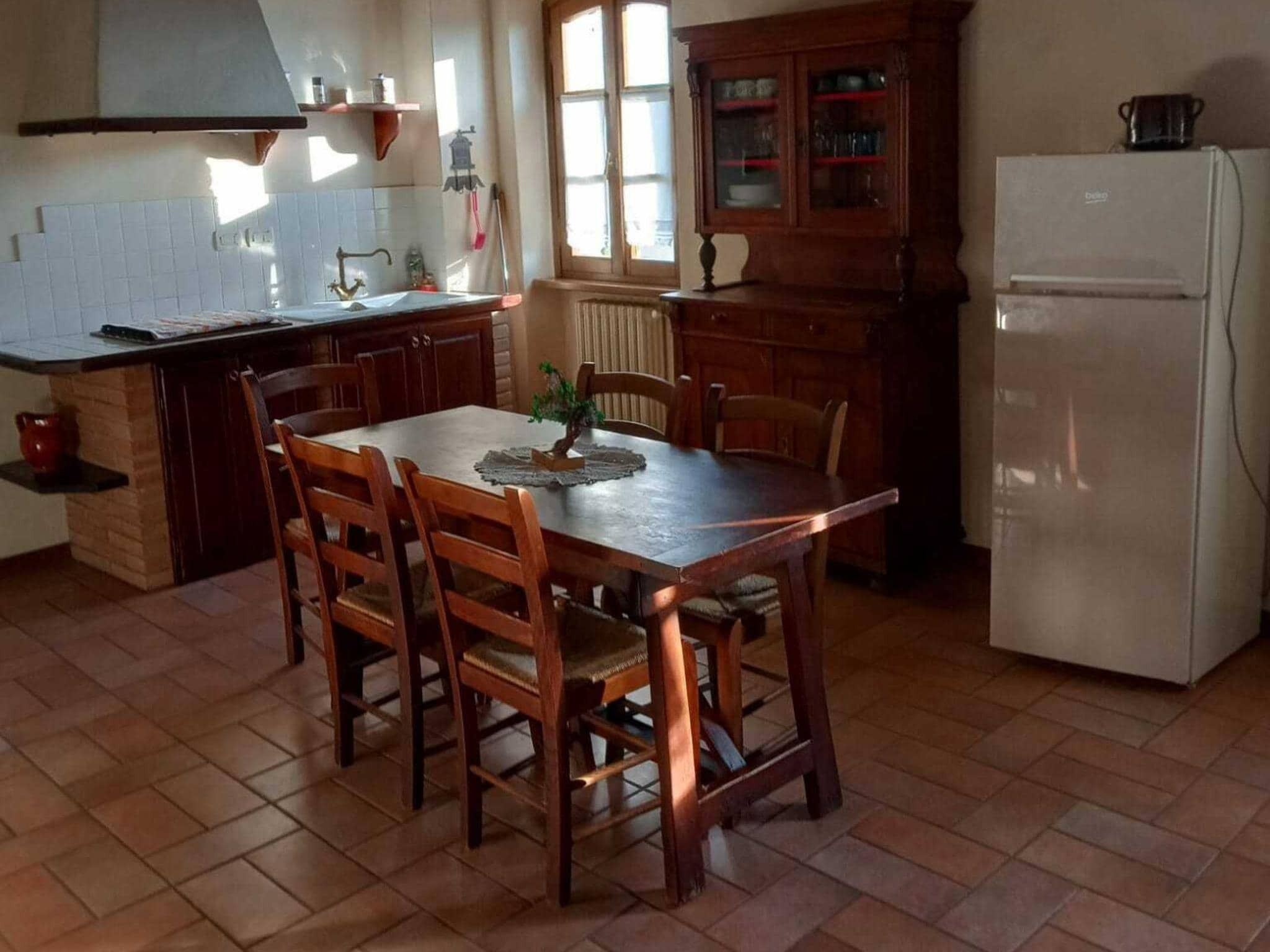A kitchen with a dining table, chairs, a refrigerator, and a cabinet.