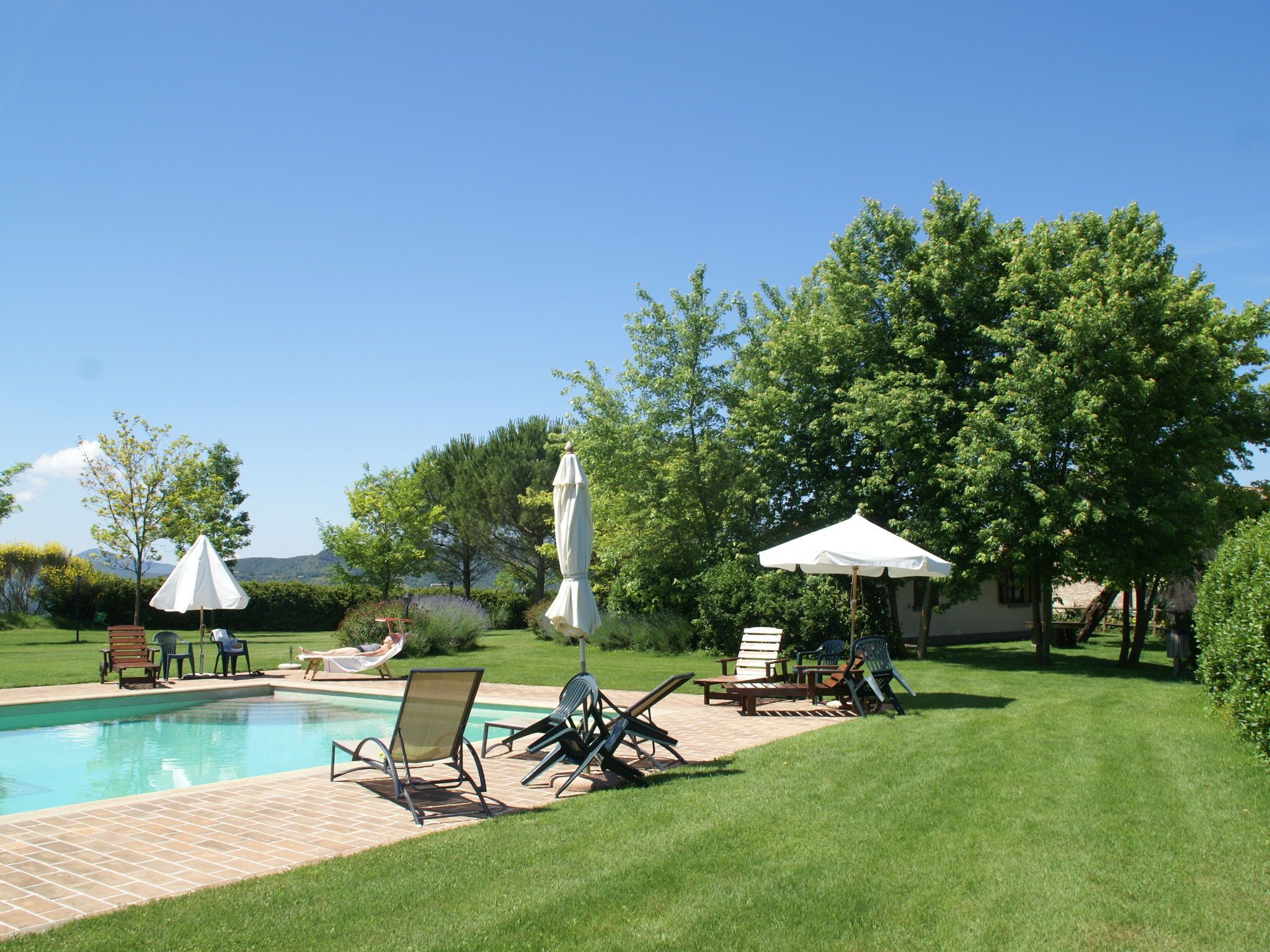 Zona junto a la piscina con sillones de descanso, sombrillas y una vista despejada del entorno con vegetación y colinas.